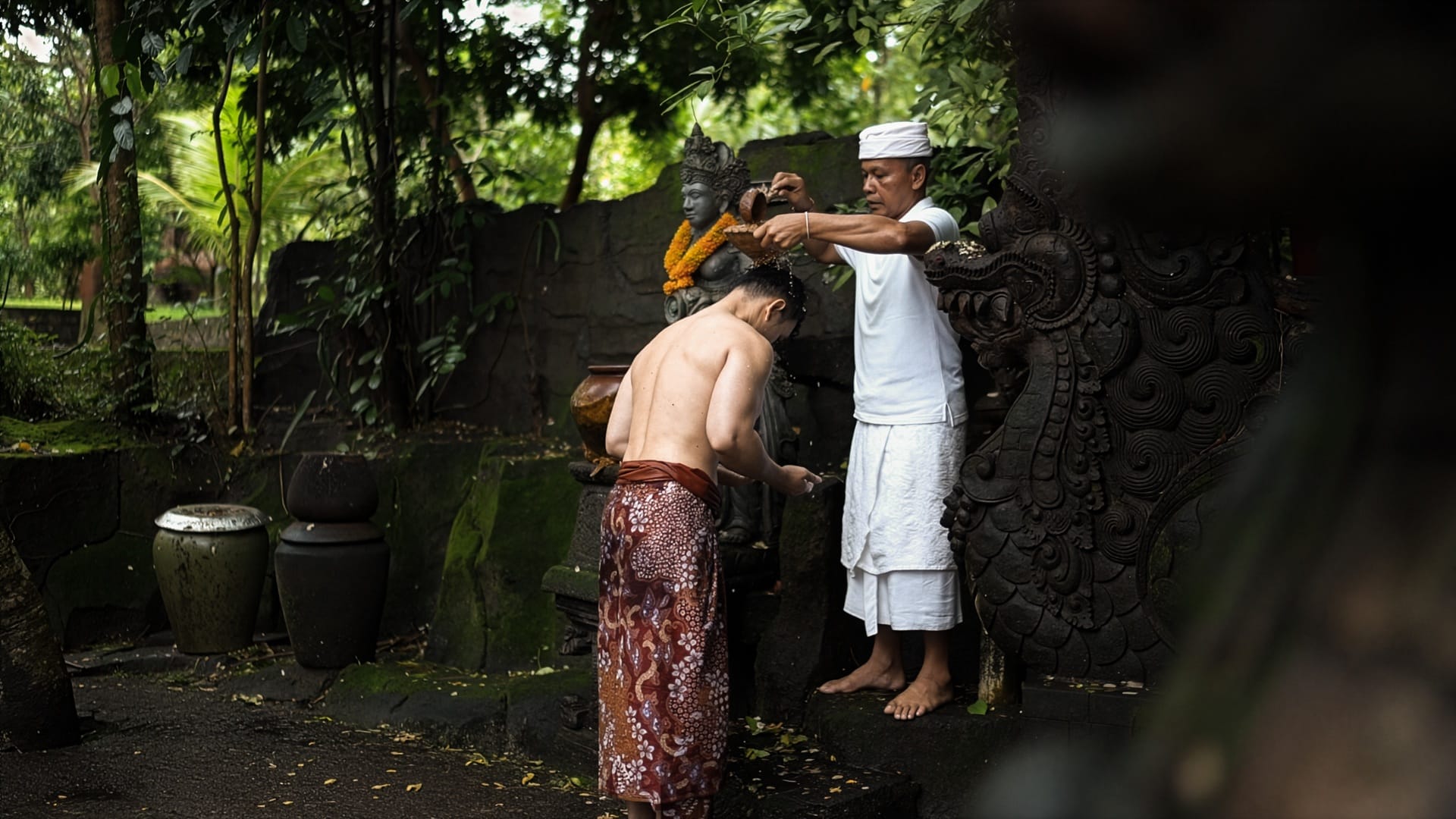 Melukat water blessing ritual performed by a Balinese priest at a moss-covered shrine